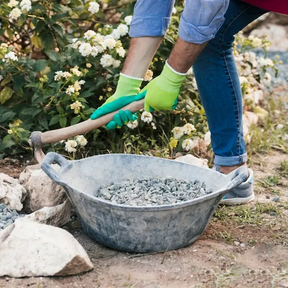 Crushed stone being scooped into a tub next to the flowers in a yard