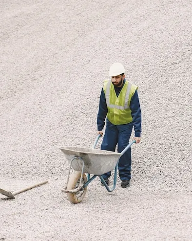 A worker with a wheelbarrow and a shovel on a big heap of crushed stone